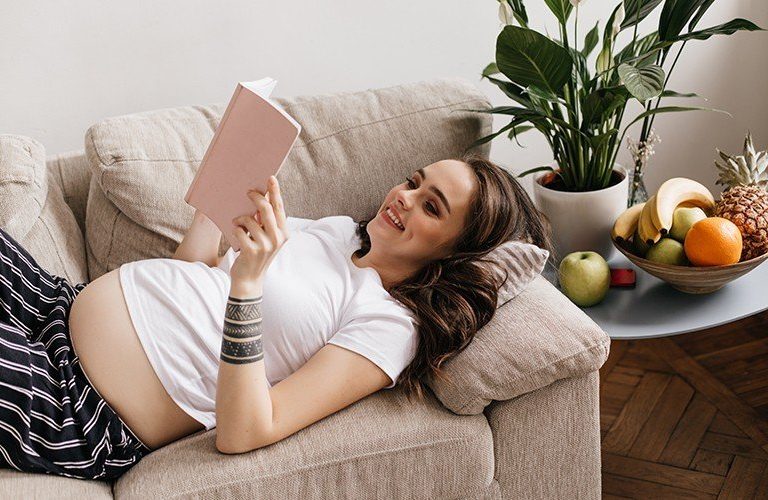 Mẹ bầu nằm trên ghế trong tư thế thoải mái và đọc sách cho thai nhi nghe.