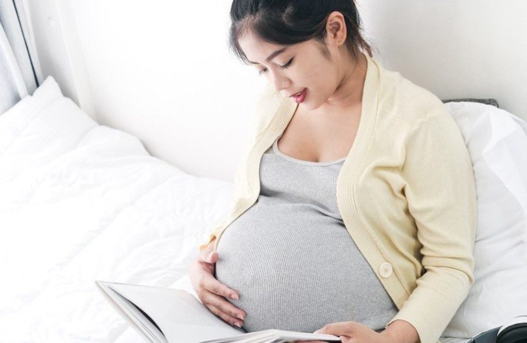Mẹ bầu ngồi trong thư thế thoải mái, vừa đọc truyện vừa vuốt ve bụng và thì thầm với thai nhi.